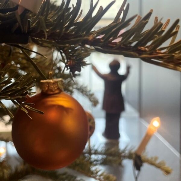 Im Hintergrund sieht man eine dirigierende wagner-Figur. Im Vordergrund eine Christbaumkugel, beleuchtet von einer Kerze am Weihnachtsbaum