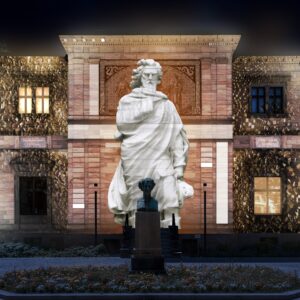 Haus Wahnfried mit beleuchteter fassade und einer der Statuen, die vor dem Haus zu sehen sind.